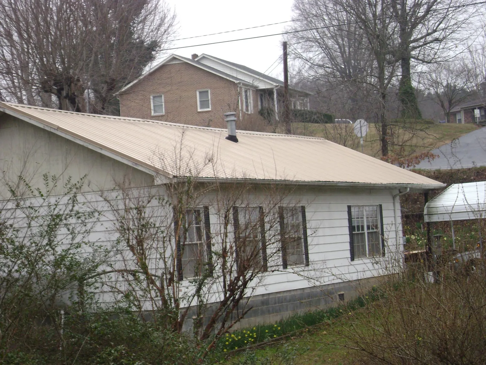 Tan metal roof on a white sided house set into a hillside — Commercial Roofing by Roofing Brothers in Middleport